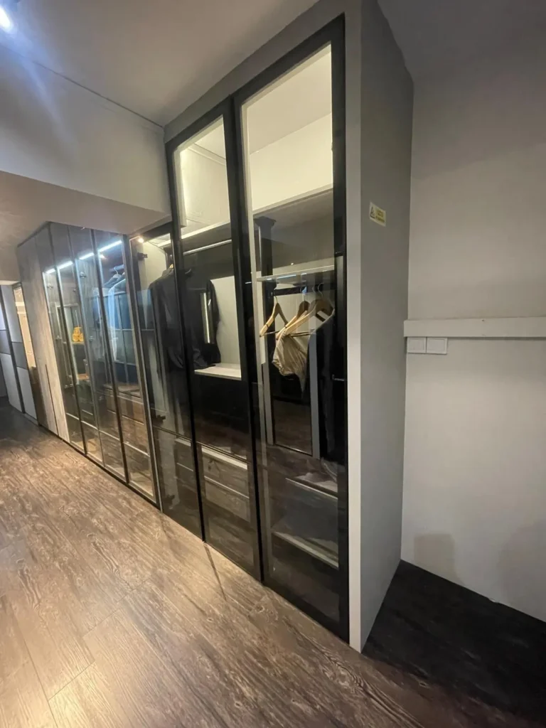 A glass closet in Singapore featuring a mirror and clothes hanging on the wall.