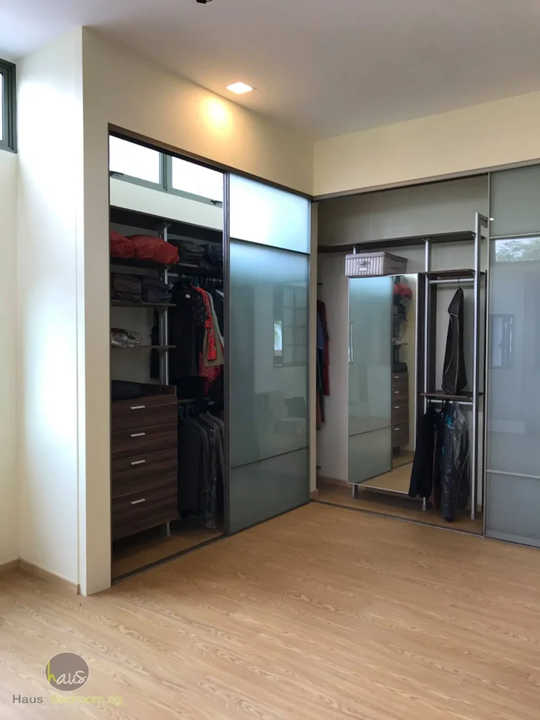 A sliding door wardrobe featuring a glass door, displaying various clothes arranged on the wall.